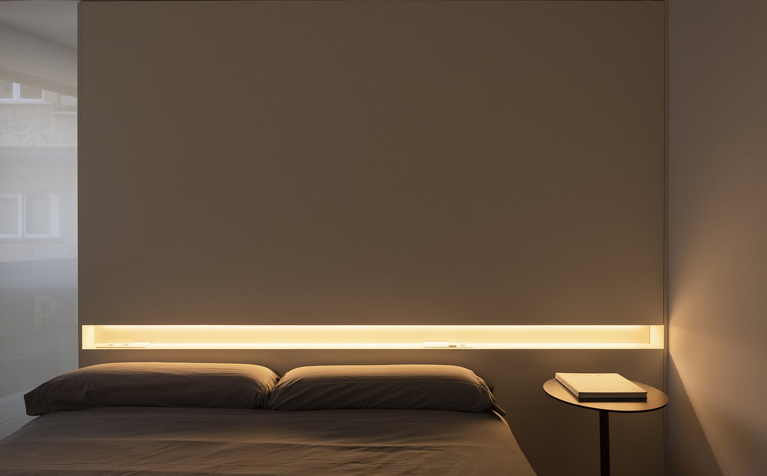 Chambre à coucher avec table de chevet, livre sur le dessus, tête de lit avec détail lumineux